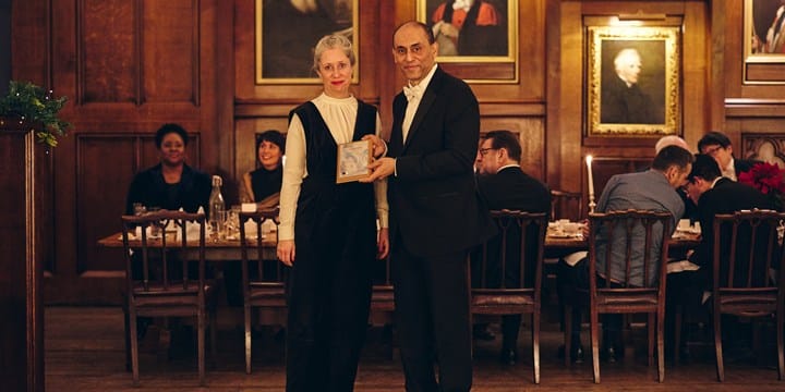 A woman in formal attire receiving an award being handed to her from a man in formal attire.