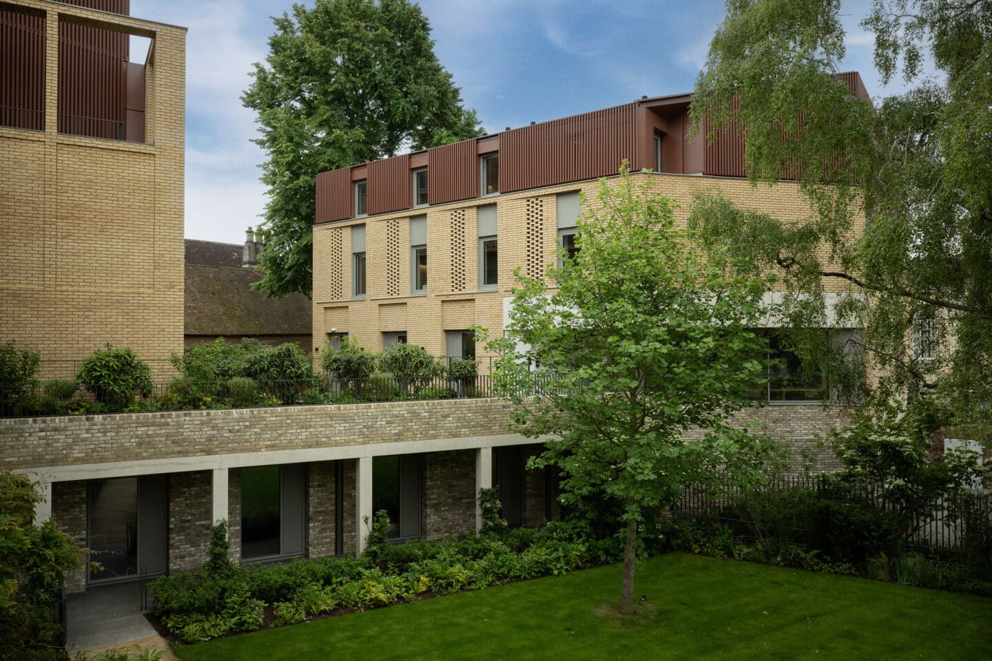 A large garden, collonnade and two brick buildings.
