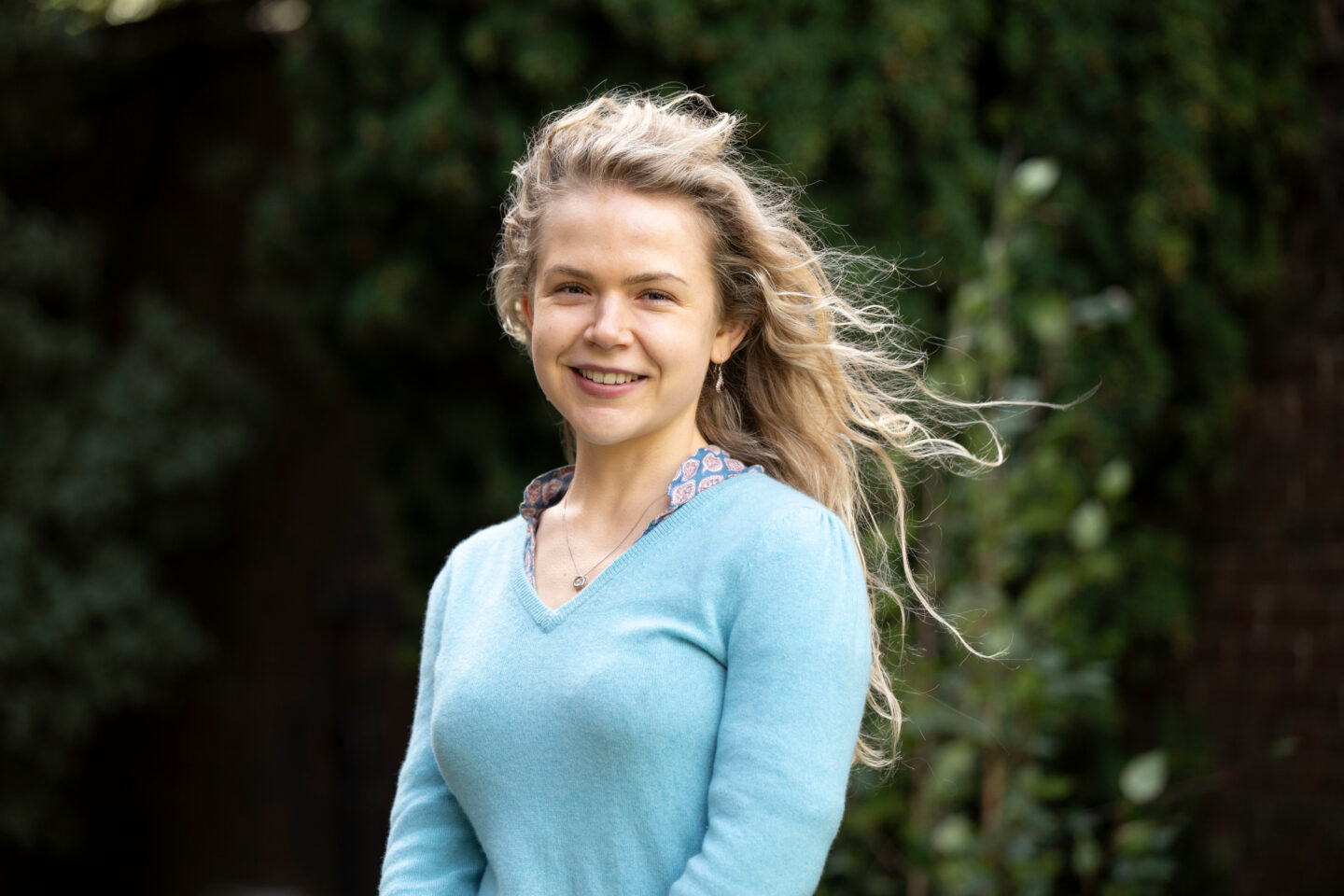 A headshot of Genista Astell standing in front of greenery