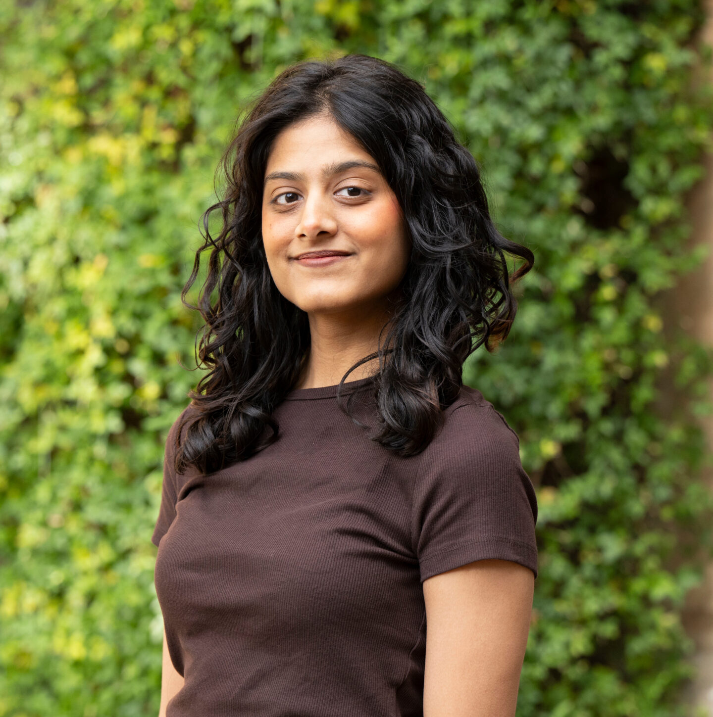 A headshot of Nadia Amina outside a brick building with vines