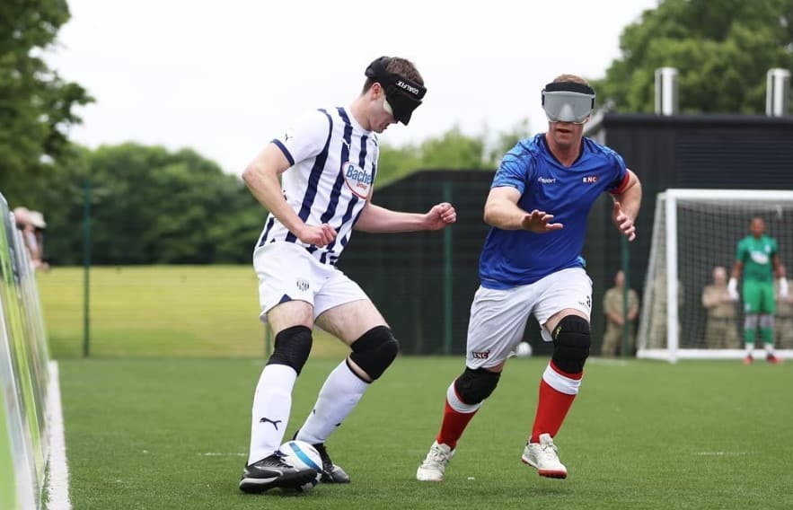 two young people in football uniforms playing blind football on an outdoor pitch