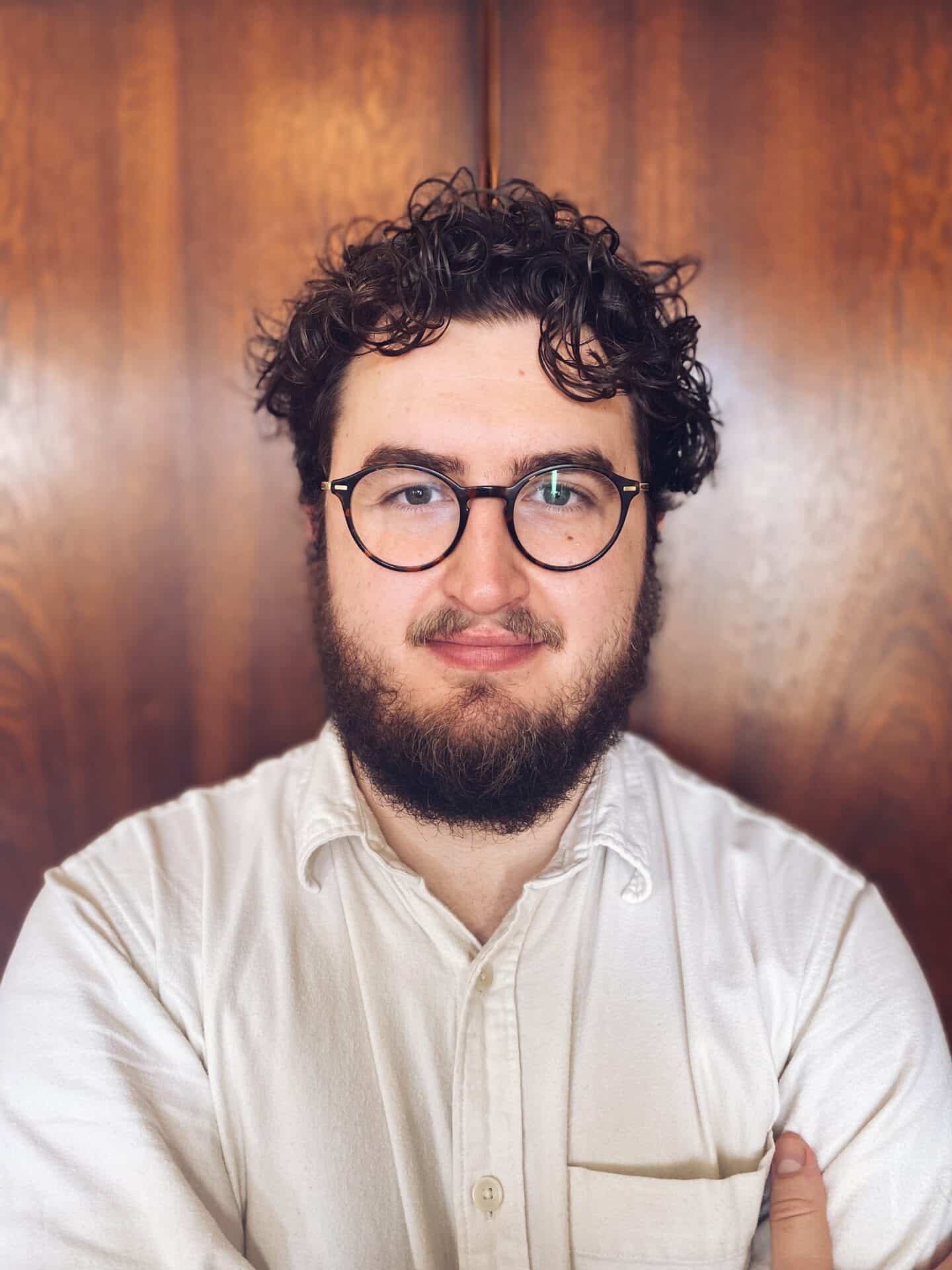 Luke Young: A headshot of a person with short hair, a beard and mustache, and large glasses