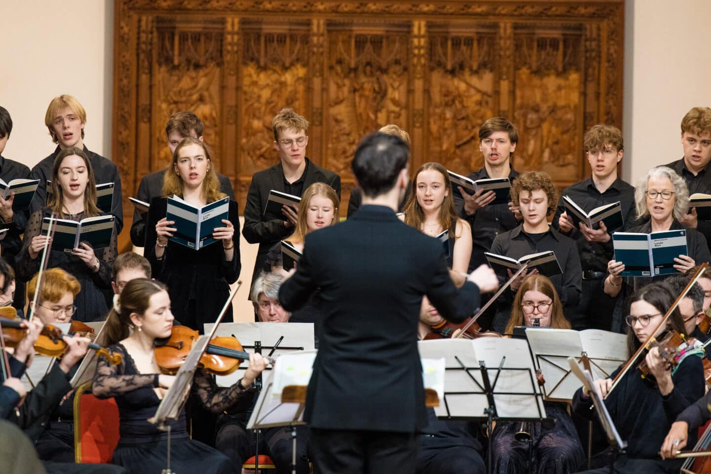 A choir and orchestra performing, with the conductor standing close to the camera