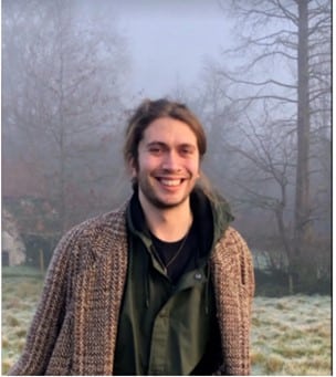 A young personstanding outside in the fog wearing a tweed jacket