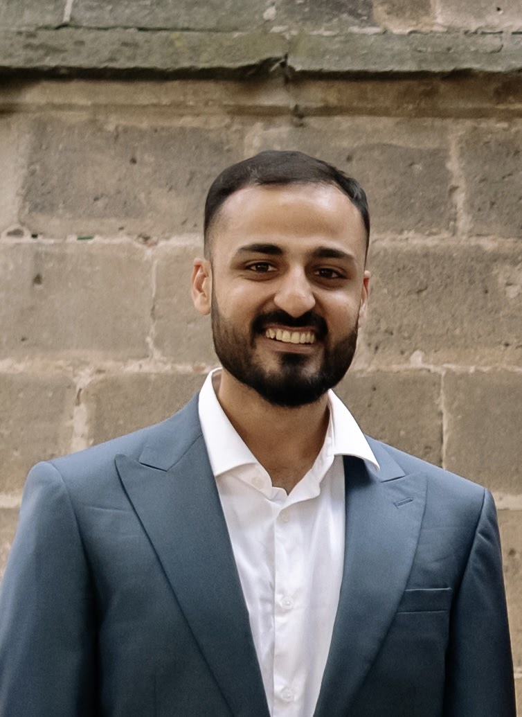 Nazem Khan - a headshot of a man wearing a grey-blue suit